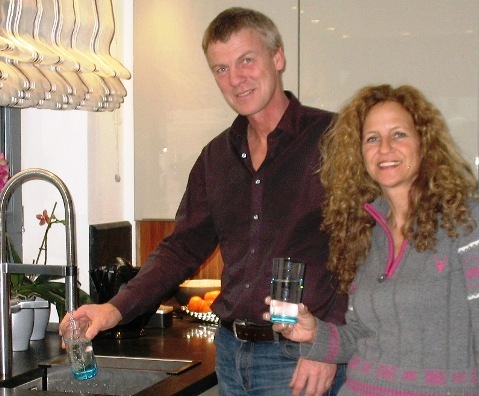 Zwei zufriedenen aqua blue Kunden stehen in ihrer Küche und lassen Leitungswasser in ihr Trinkglas laufen.