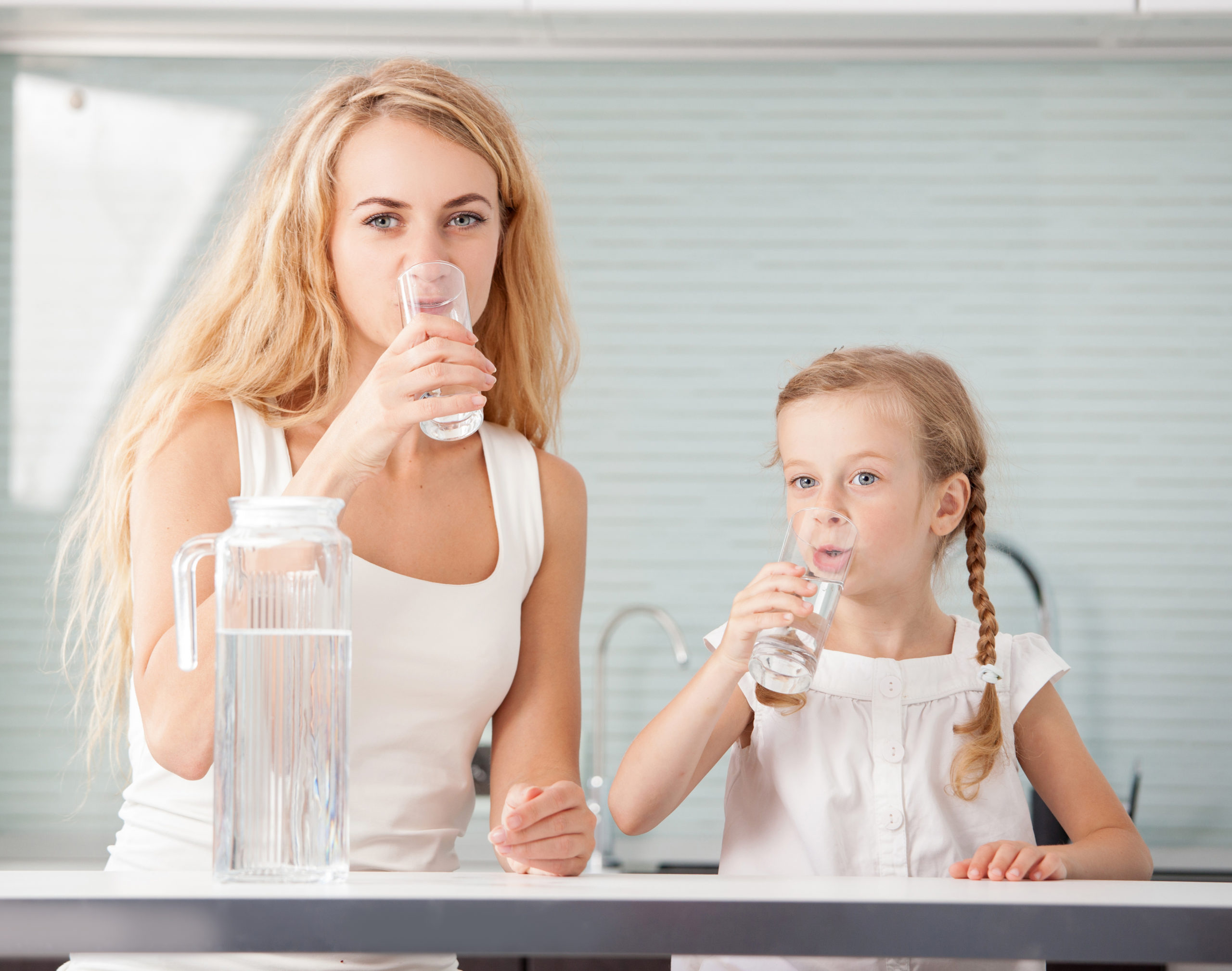 Blonde Mutter und Tochter trinken Wasser aus einem Glas in der küche.