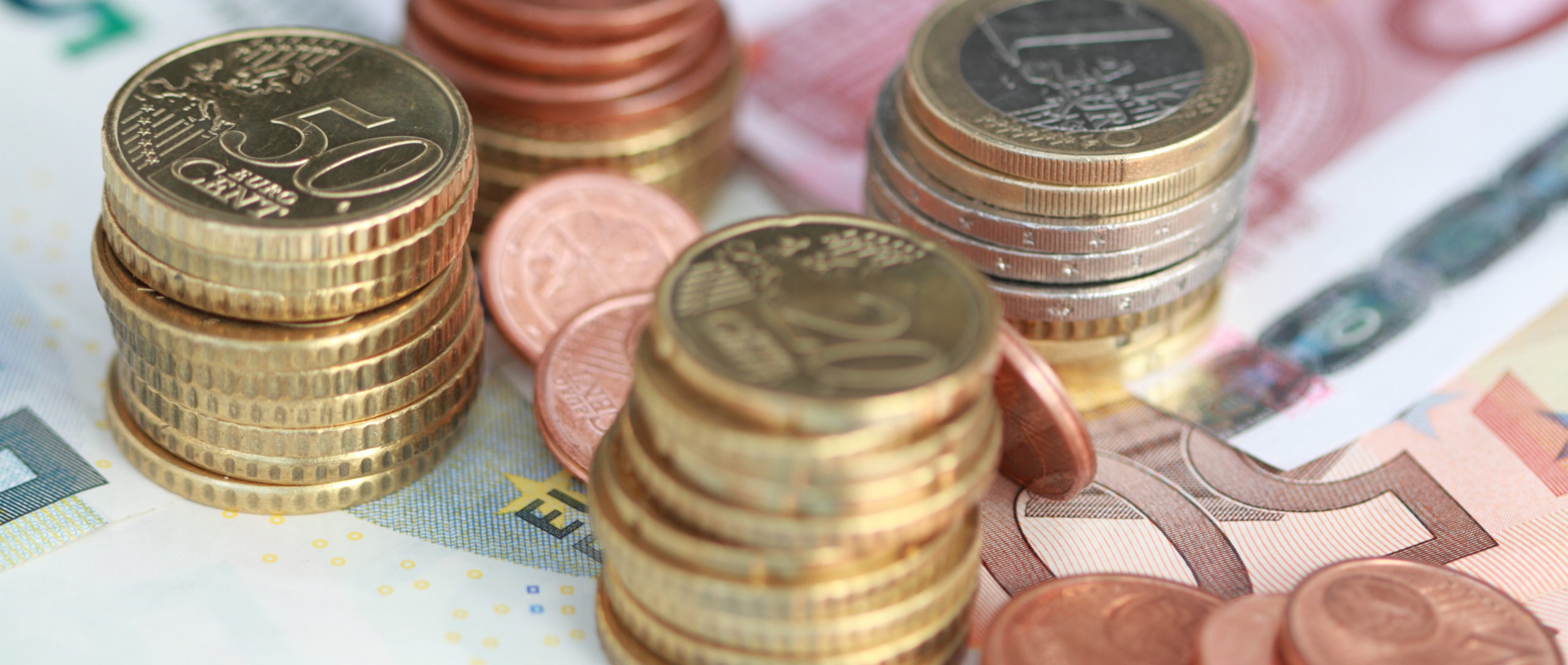 Geld sparen mit Wasserenthärtungsanalge Ein 50€-, 10€- und 5€-Schein liegen auf dem Tisch. Darauf liegen Stapel von 50 Cent Stücken, 20 Cent Stücken und 1€ und 2€ Stappel