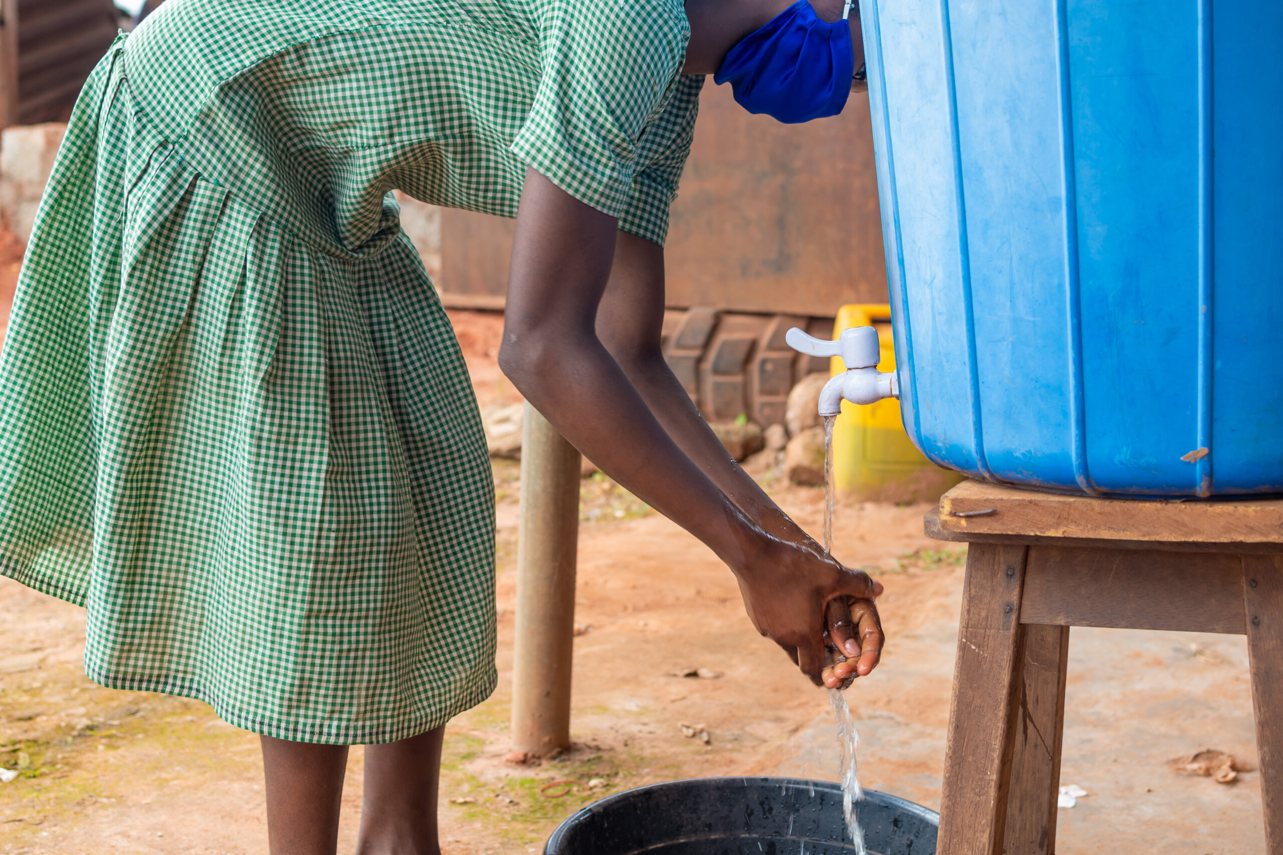 kid washing her hand from a rubber container put in place for hand washing
